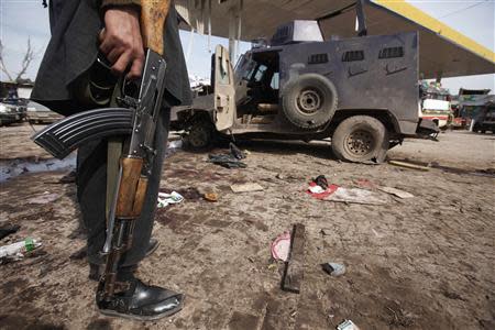 A security official stands near a damaged vehicle at the site of a bomb blast in the outskirts of Peshawar March 14, 2014. REUTERS/Fayaz Aziz