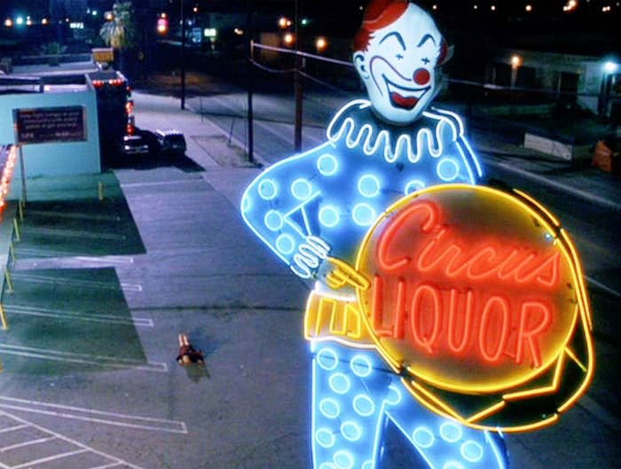 A liquor store neon light and a woman lying on the ground in a parking lot
