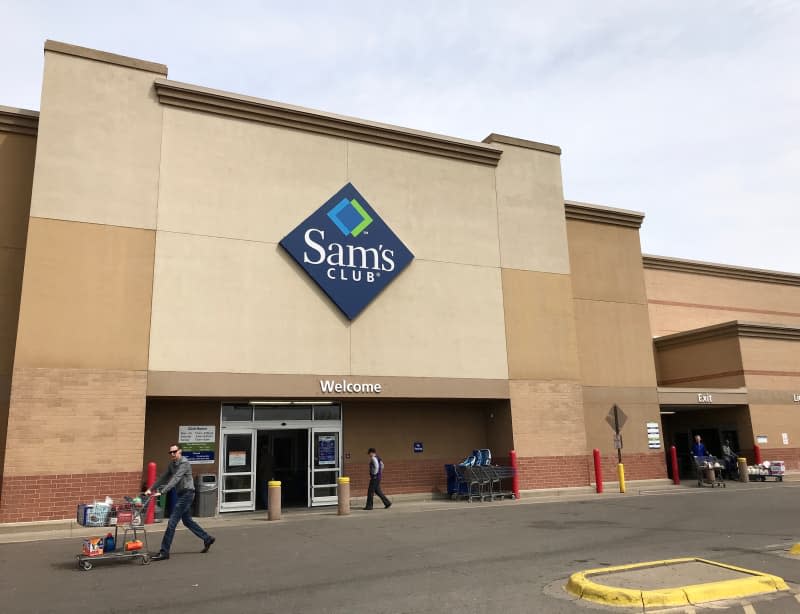 The exterior of a Sam’s Club store with a shopper walking in and away from it.