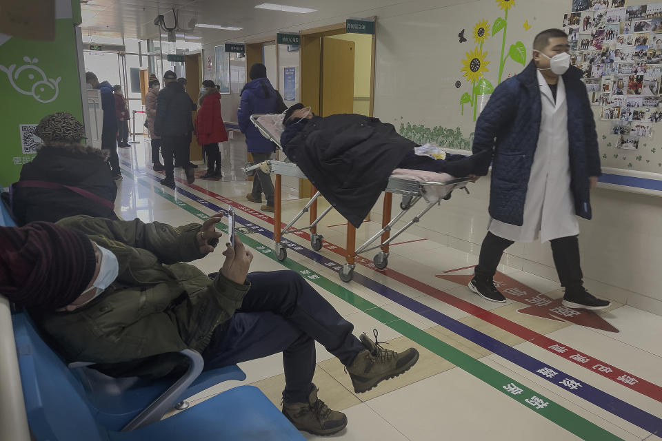 A man browses his smartphone as an elderly patient is wheeled to an emergency hall in a hospital in Beijing, Saturday, Jan. 7, 2023. China has suspended or closed the social media accounts of more than 1,000 critics of the government's policies on the COVID-19 outbreak, as the country moves to further open up. (AP Photo/Andy Wong)