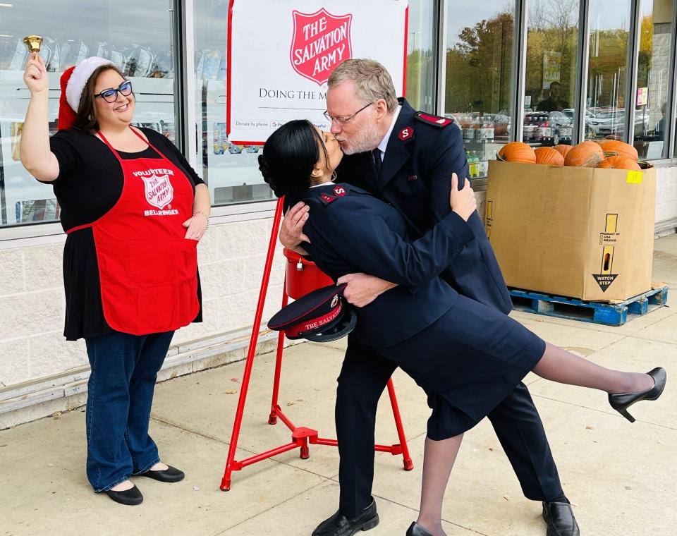 Sonya Richards rings a bell as Salvation Army Maj. Robert Watson plants a kiss on his wife, Capt. Anita Albert-Watson, as they promote Kiss at the Kettle during the Red Kettle Campaign.