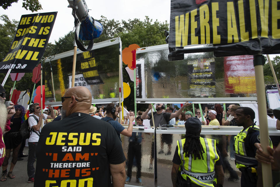 FILE - Religious protesters from a street preachers association watch a group of pro-LGBTQ activists erect a series of boards they call "hate shields" intended to muffle megaphones and serve to reflect the counter-protesters' images in Atlanta, Oct. 12, 2019. The march was part of the annual Gay Pride Festival. Hate speech and threats of violence targeting transgender people and other LGBTQ individuals is thriving on social media and spurring fears of more violence. (AP Photo/Robin Rayne, File)