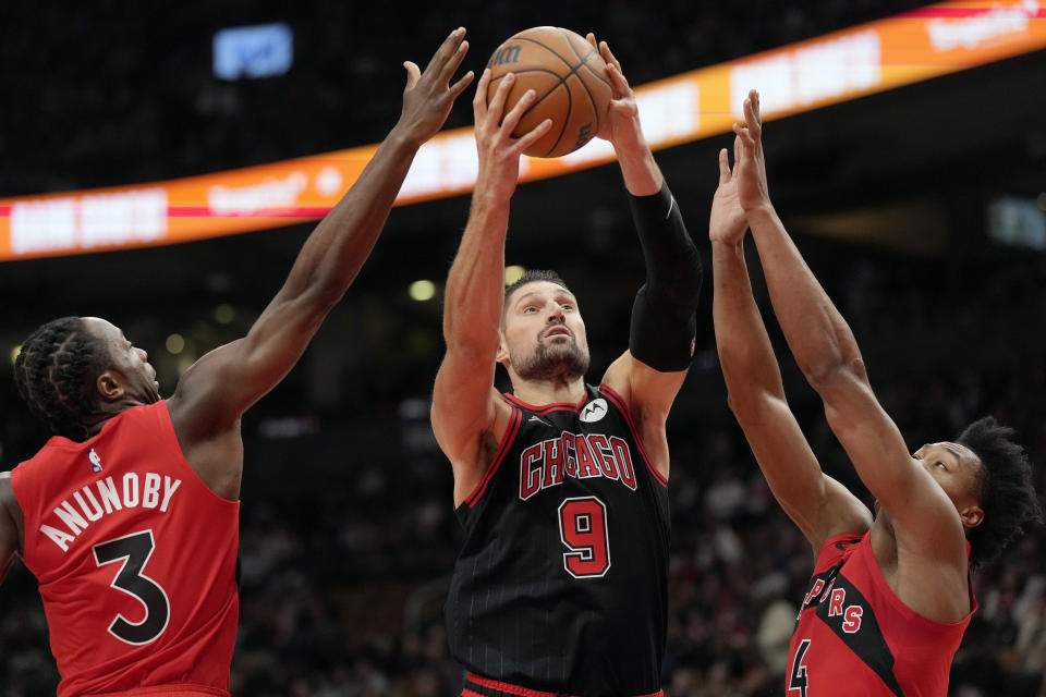 Chicago Bulls center Nikola Vucevic (9) goes for a layup as Toronto Raptors forward O.G. Anunoby (3) and Scottie Barnes (4) defend during first-half NBA basketball game action in Toronto, Sunday, Nov. 6, 2022. (Frank Gunn/The Canadian Press via AP)