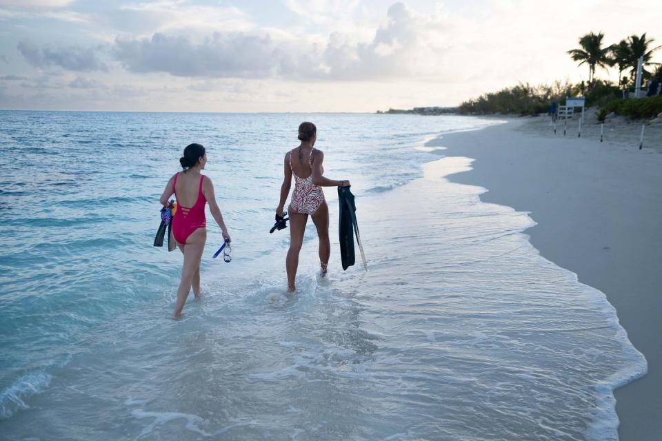 two women carrying snorkeling gear along a beach