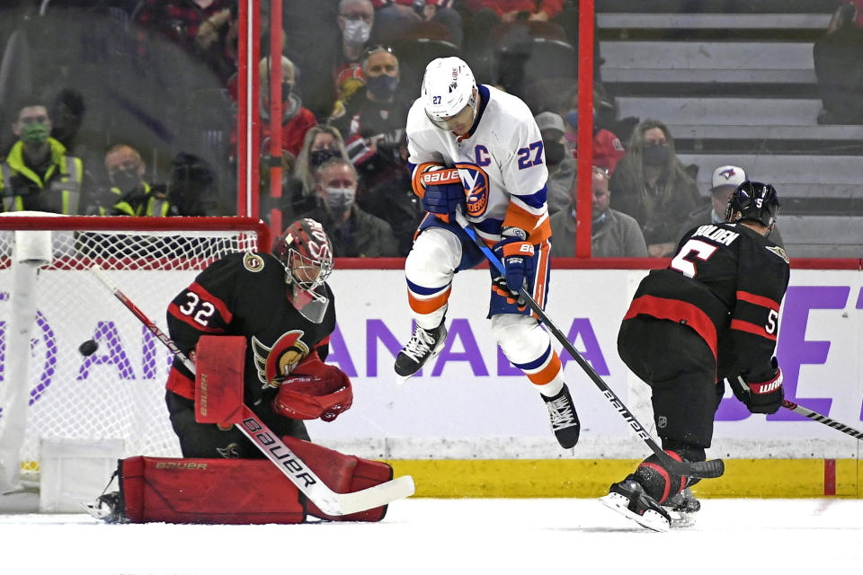 The puck goes wide of the net of Ottawa Senators goaltender Filip Gustavsson (32) as New York Islanders center Anders Lee (27) jumps clear of the shot during the second period of an NHL hockey game Tuesday, Dec. 7, 2021, in Ottawa, Ontario. (Justin Tang/The Canadian Press via AP)