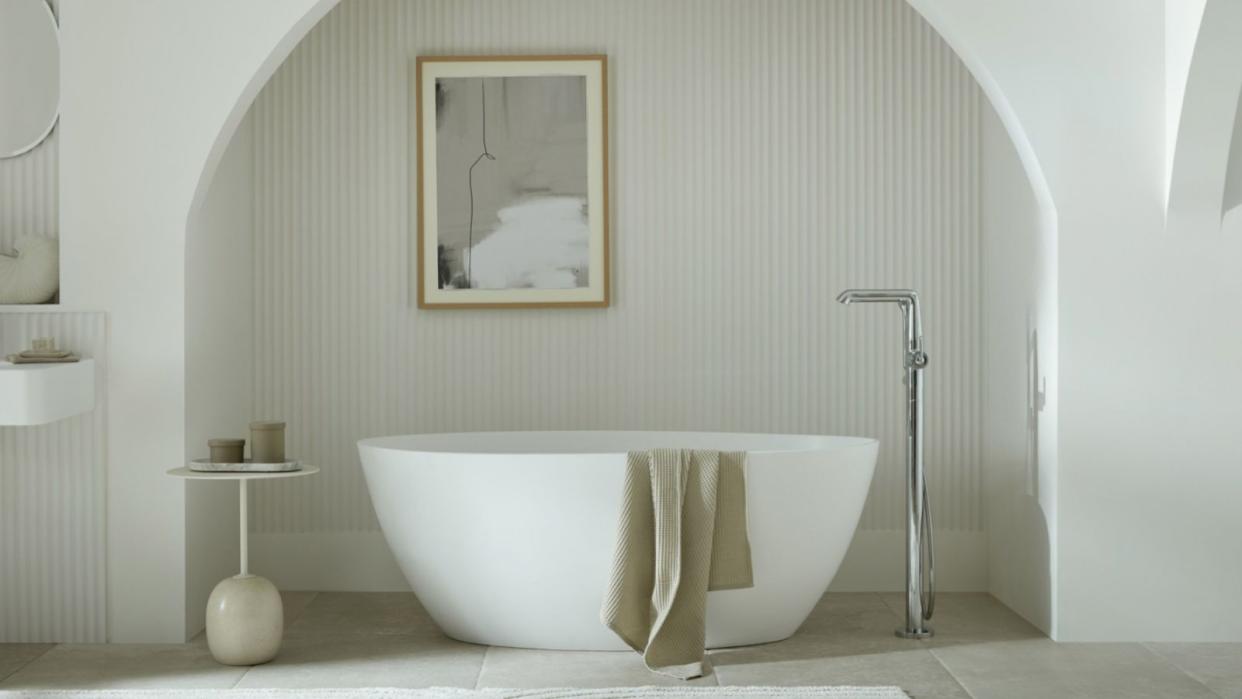  All white bathroom with a curved free standing tub in an alcove 