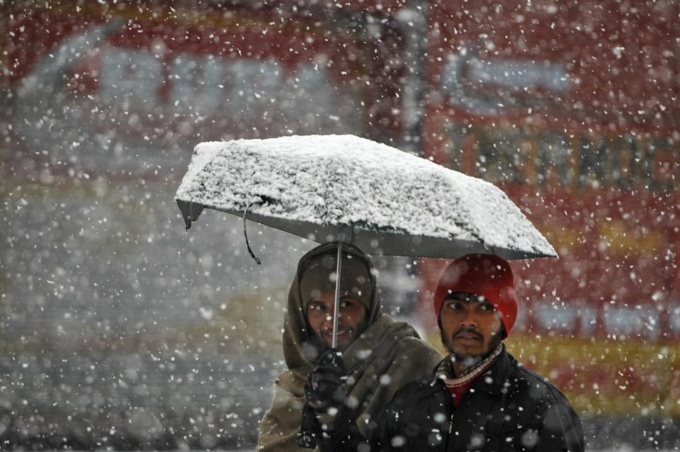 Men walk under an umbrella during snowfall on a cold winter morning in Srinagar