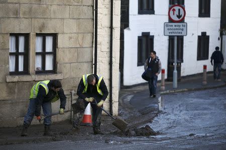 Men clear silt outside a home after flooding in the town of Mytholmroyd, northern England, December 27, 2015. REUTERS/Andrew Yates