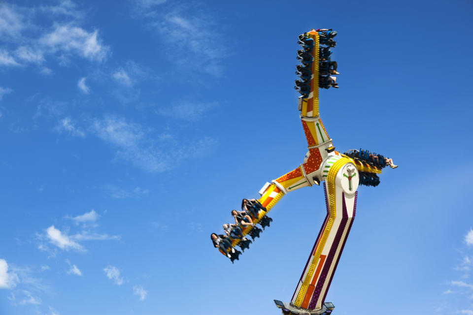 People are enjoying a thrilling ride on a large amusement park ride that spins in the air against a clear blue sky