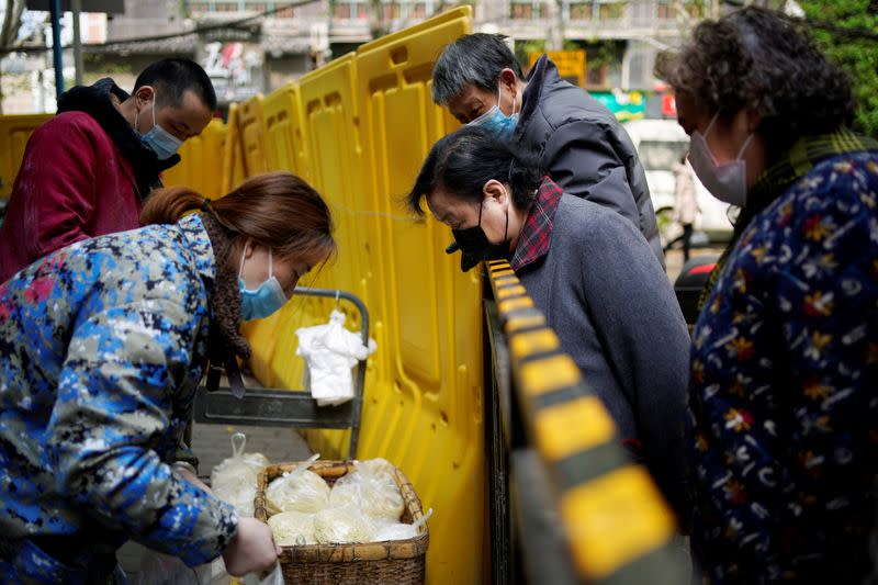 Residents wearing face masks pay for noodles at a residential area blocked by barriers in Wuhan