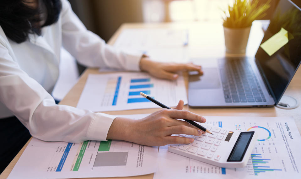 Office worker or Business women using calculator, laptop computer, and chart report paper, statistic income on the table in the sunset at the office workplace.