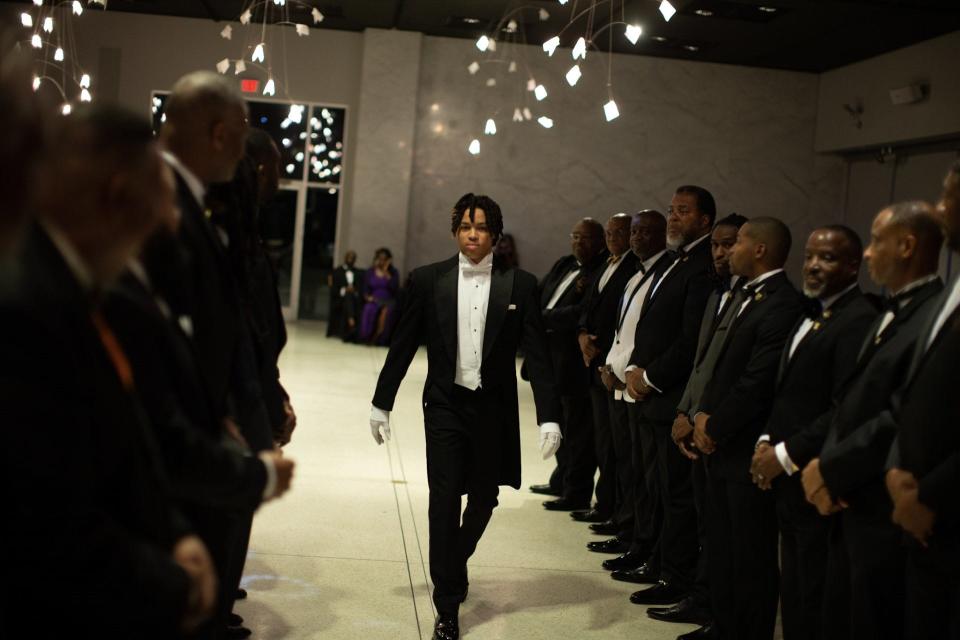 A participant in the Epsilon Rho Lambda chapter of Alpha Phi Alpha's I Am A.L.P.H.A. program walks through a tunnel formed by fraternity alumni at its June 2023 Beautillion event.
