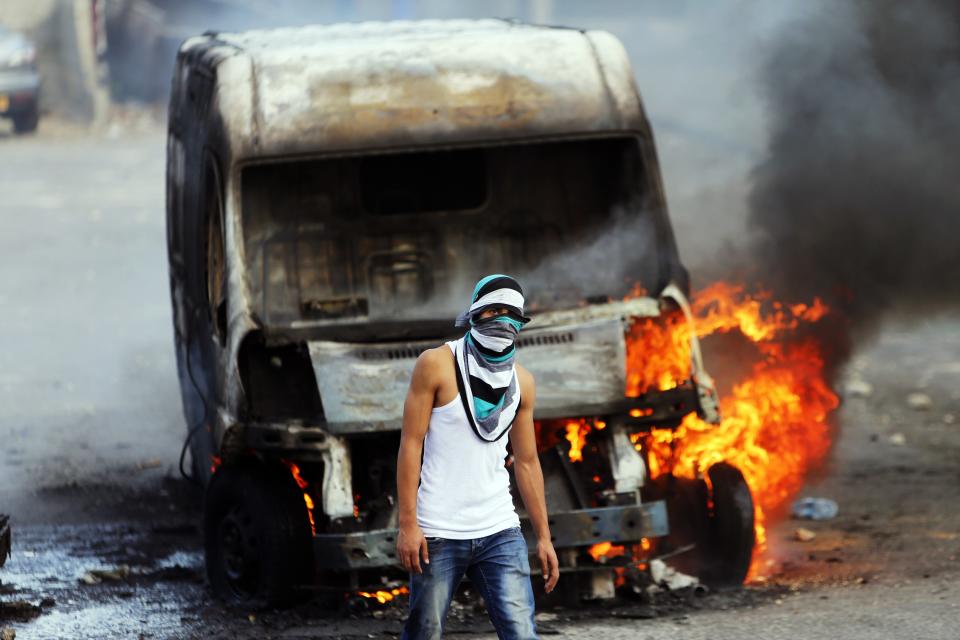 A Palestinian protester stands in front of a car of an Israeli that was set on fire by the protesters during clashes with Israeli security forces in east Jerusalem October 30, 2014. Israeli police on Thursday shot dead a 32-year-old Palestinian man suspected of having tried hours earlier to kill a far-right Jewish activist, leading to fierce clashes in East Jerusalem and fears of a new Palestinian uprising. The Al-Aqsa compound, or Temple Mount, which is a central cause of the latest violence, was closed to all visitors as a security precaution. It was the first full closure of the site, venerated by both Jews and Muslims, in 14 years. REUTERS/Ammar Awad (JERUSALEM - Tags: POLITICS CIVIL UNREST RELIGION TPX IMAGES OF THE DAY)