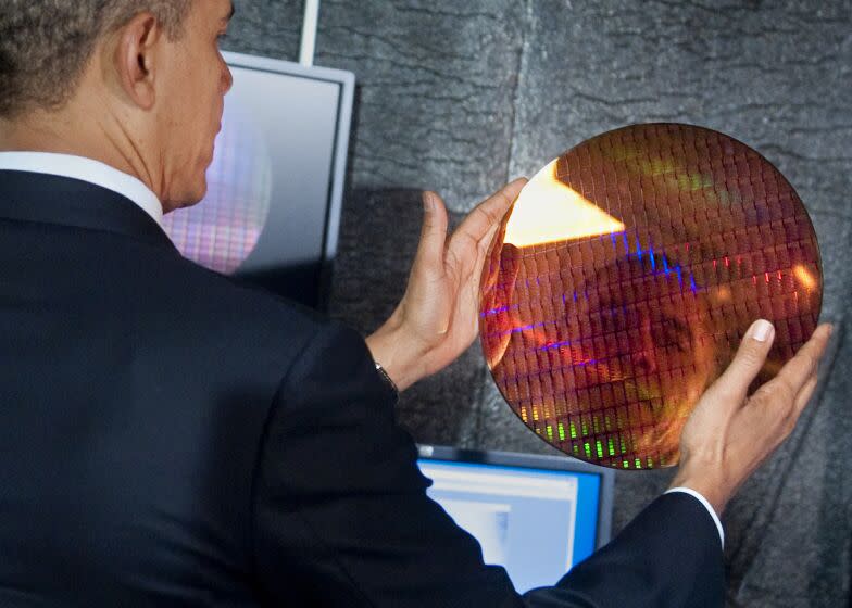 US President Barack Obama looks at his reflection as he holds an Intel wafer made of microchips