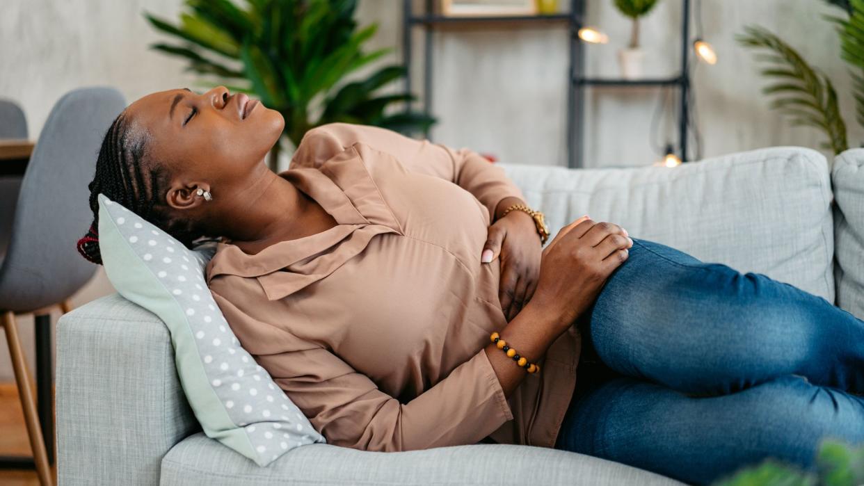 Young black woman lying on the sofa and having period cramps.