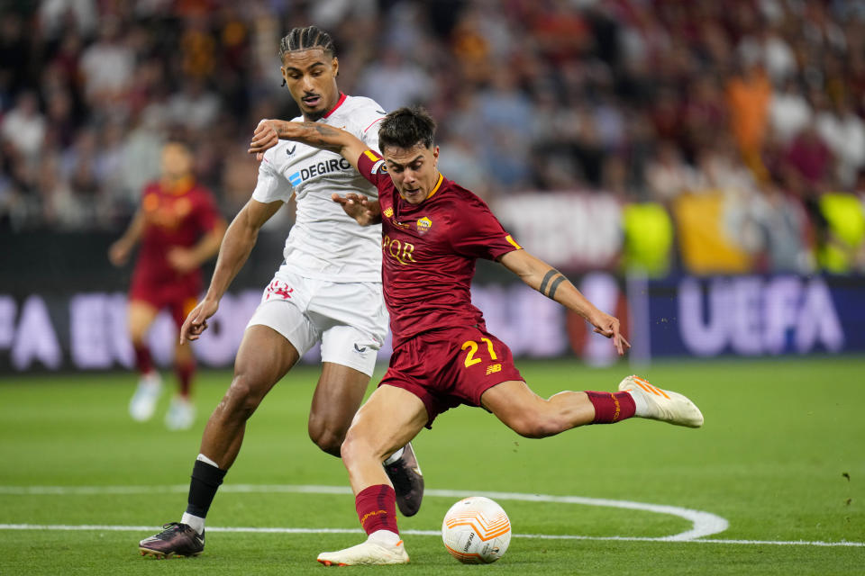 Roma's Paulo Dybala scores the opening goal past Sevilla's Loic Bade, left, during the Europa League final soccer match between Sevilla and Roma, at the Puskas Arena in Budapest, Hungary, Wednesday, May 31, 2023. (AP Photo/Petr David Josek)