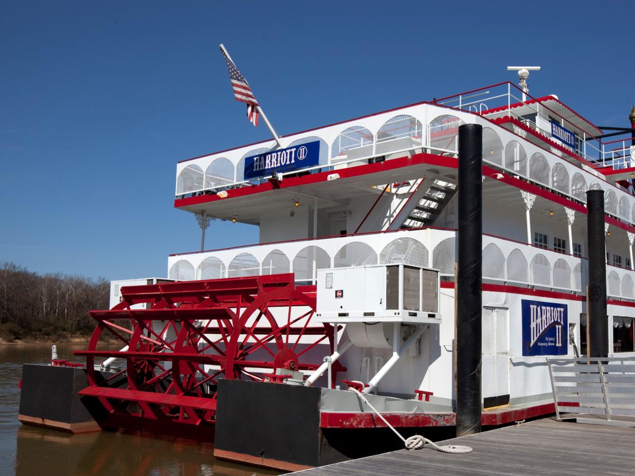 A red and white riverboat on the Alabama river beside a wooden dock