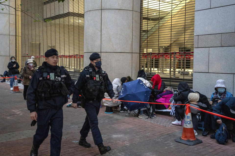 Policemen patrol walking past people who were waiting behind a police barricade line outside West Kowloon Magistrates' Courts where Jimmy Lai's trial will be held in Hong Kong, Monday, Dec. 18, 2023. (AP Photo/Vernon Yuen)