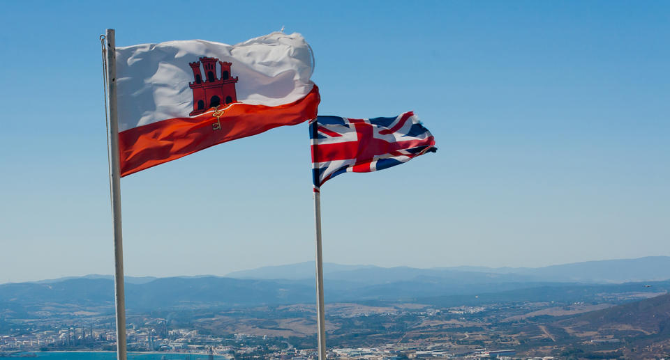 The Gibraltar flag (white with a red bottom and a red castle) on a flag post in front of the UK's flag.