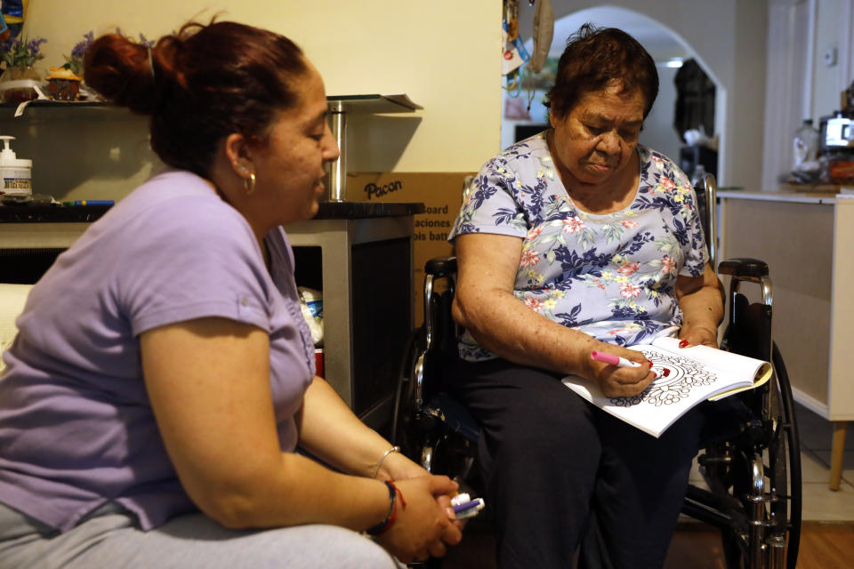 Eugenia Rodriguez, left, looks toward her 84-year-old, non-citizen mother, Francisca Perez, who colors a book, a part of her regular exercise to recover rheumatoid arthritis, Wednesday, June 30, 2021, in their house in Chicago's Little Village neighborhood. Rodriguez hasn't been eligible for insurance coverage after overstaying a visitor visa from Mexico. She used to wake up every two or three hours at night to check on her mother. Since getting health insurance through the Illinois program, her mother has all the medications she needs. (AP Photo/Shafkat Anowar)