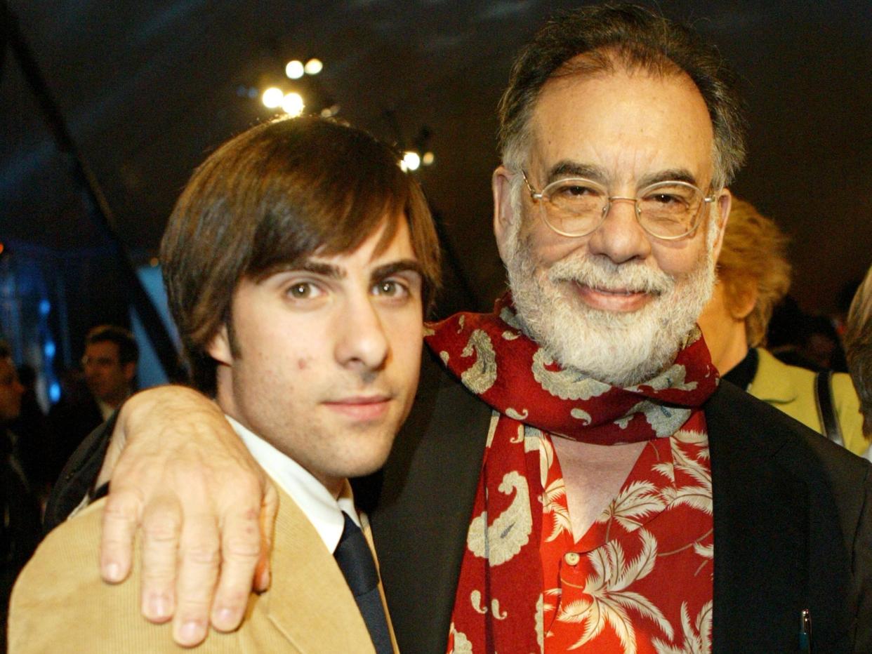 jason schwartzman and francis ford coppola two decades ago posing for a photo. coppola has his arm around schwartzman's shoulder, and both are smiling. schwartzman has slightly long hair and is wearing a beige jacket, and coppola is in a black jacket with a red printed shirt and scarf