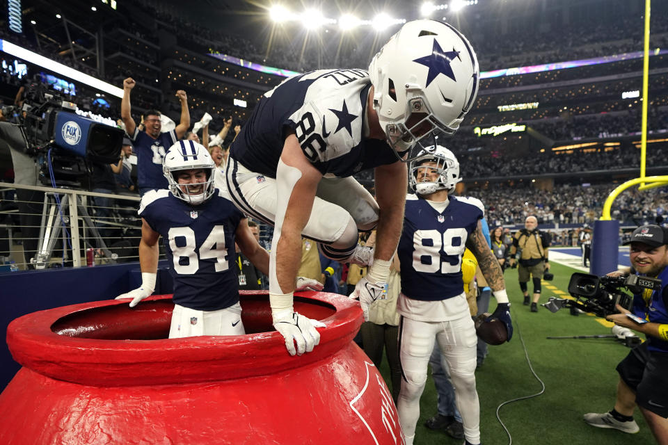 Dallas Cowboys' Dalton Schultz (86) jumps out of a Salvation Army kettle while celebrating Peyton Hendershot's (89) touchdown along with Sean McKeon (84) during the second half of an NFL football game against the New York Giants Thursday, Nov. 24, 2022, in Arlington, Texas. (AP Photo/Tony Gutierrez)