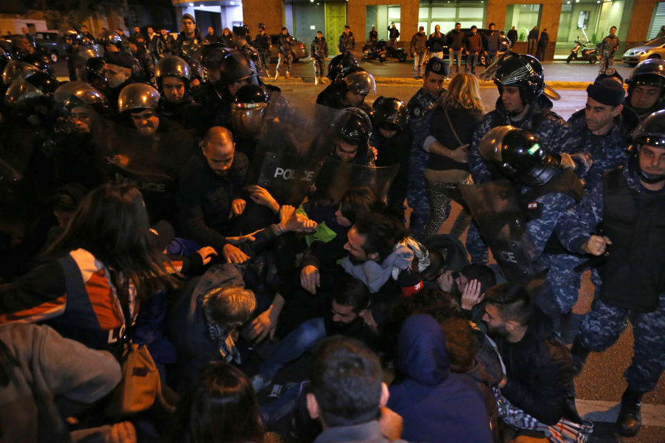 Anti-government protesters lie on a road, as they scream and hold each others while riot police try to remove them and open the road, in Beirut, Lebanon, Wednesday, Dec. 4, 2019. Protesters have been holding demonstrations since Oct. 17 demanding an end to widespread corruption and mismanagement by the political class that has ruled the country for three decades. (AP Photo/Bilal Hussein)