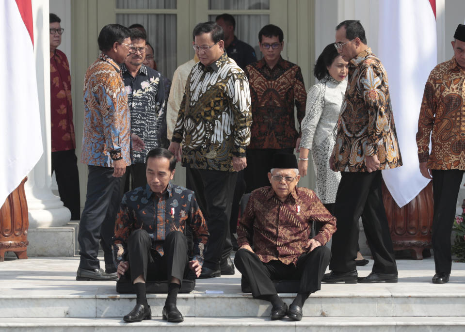 Newly appointed Defense Minister Prabowo Subianto, center, walks past Indonesian President Joko Widodo, seated left, his former rival in last April's election and Vice President Ma'ruf Amin, seated right, during the announcement of the new cabinet ministers at Merdeka Palace in Jakarta, Indonesia, Wednesday, Oct. 23, 2019. (AP Photo/Dita Alangkara)