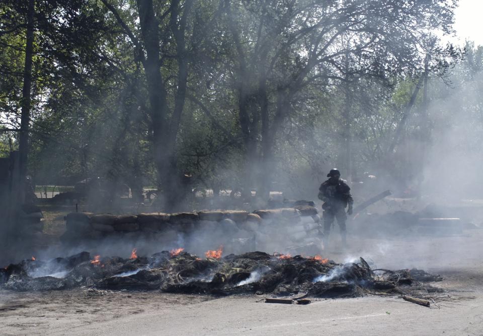 Smoke billows from burning tires around a Ukrainian special forces soldier at a checkpoint following an attack by Ukrainian troops outside Slovyansk, Ukraine, Thursday, April 24, 2014. Ukrainian government troops moved against pro-Russia forces in the east of the country on Thursday and killed at least two of them in clashes at checkpoints manned by the insurgents, the government and insurgents said. Russian President Vladimir Putin decried what he described as a "punitive operation." (AP Photo/Mika Velikovskiy)