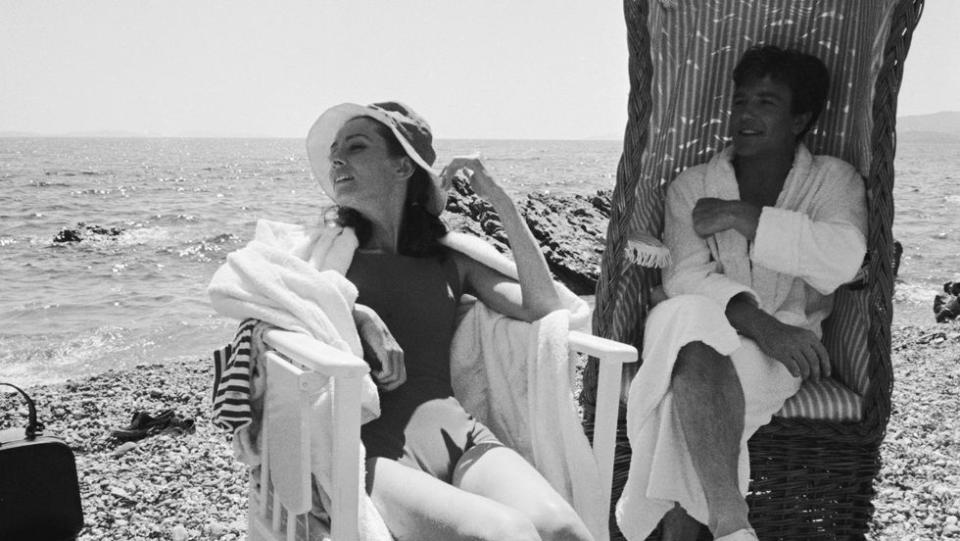 <p>Audrey Hepburn soaks up the sun while Albert Finney relaxes in the shade during the filming of <em>Two for the Road</em> in 1966.</p>