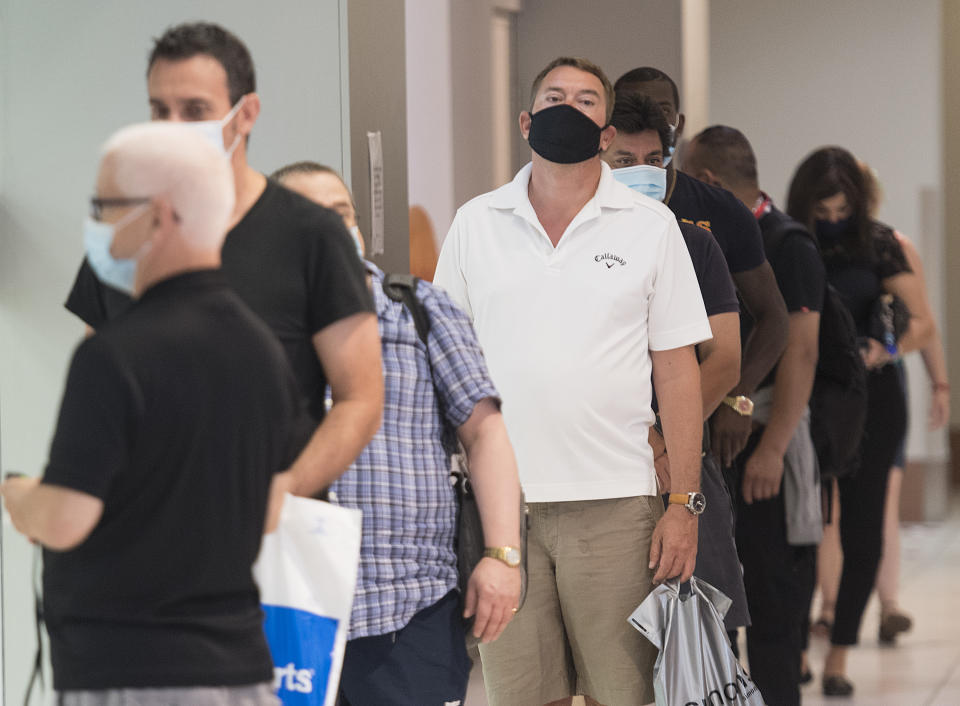 People wear face masks as they wait to enter a department store in Montreal, Saturday, July 18, 2020, as the COVID-19 pandemic continues in Canada and around the world. The wearing of masks or protective face coverings is mandatory in Quebec as of today. THE CANADIAN PRESS/Graham Hughes