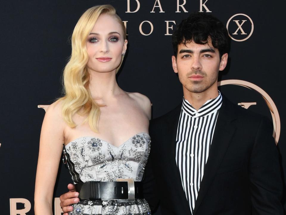 Sophie Turner in a striped dress and heels standing taller than Joe Jonas in a striped shirt and suit.