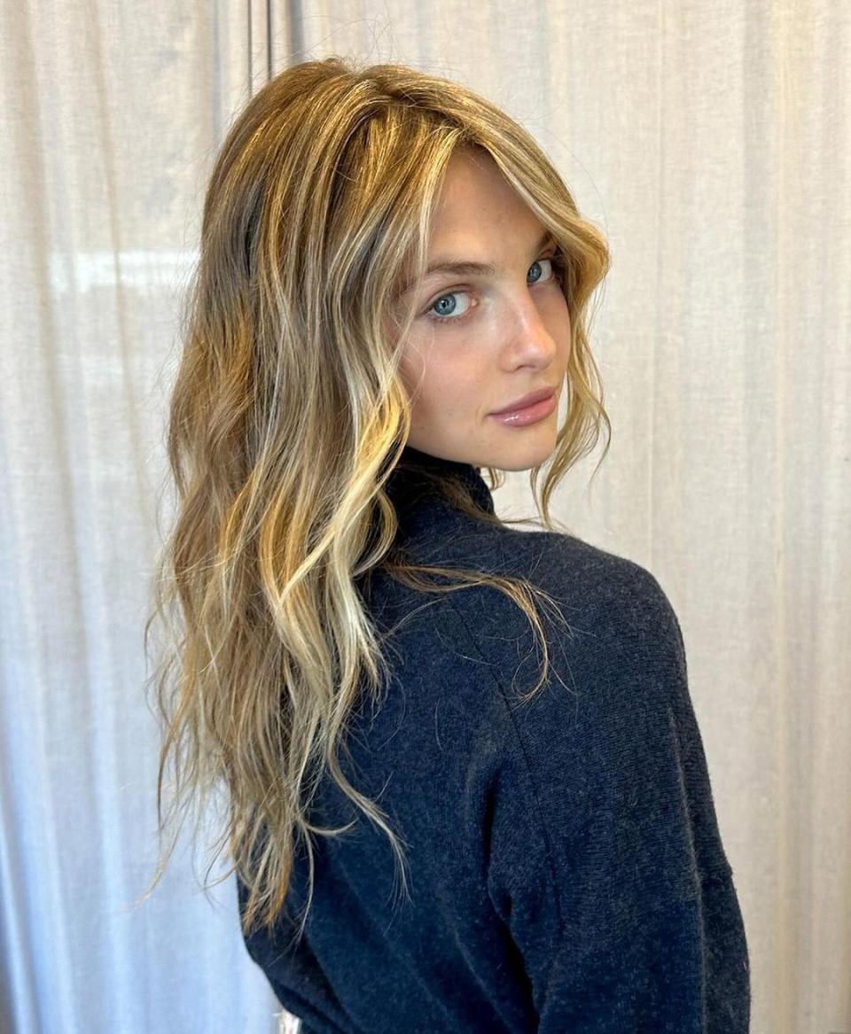 A waist-up photo of a white woman with blonde hair and blue eyes looking into the camera with freshly highlighted hair.