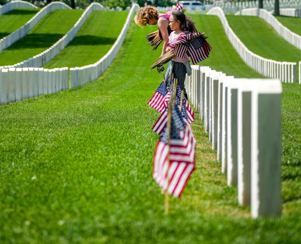 Laurie Kaluzny places flags with her boyfriend's granddaughter, Ava Brannin, 7, on Saturday at Wood National Cemetery in Milwaukee. Placing the flags ahead of Memorial Day is an annual tradition for volunteers and cemetery workers.