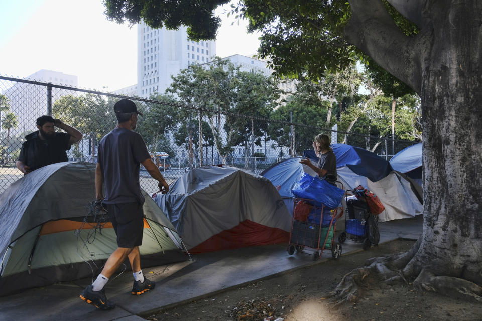 FILE - In this Monday, July 1, 2019 file photo, homeless people move their belongings from a street along side of Los Angeles City Hall as crews prepared to clean the area. Members of the Trump administration are visiting Los Angeles to get a firsthand look at the city's sprawling homeless encampments, while President Donald Trump has directed his staff to develop policy options to address the national crisis of people living on the streets. (AP Photo/Richard Vogel, file)