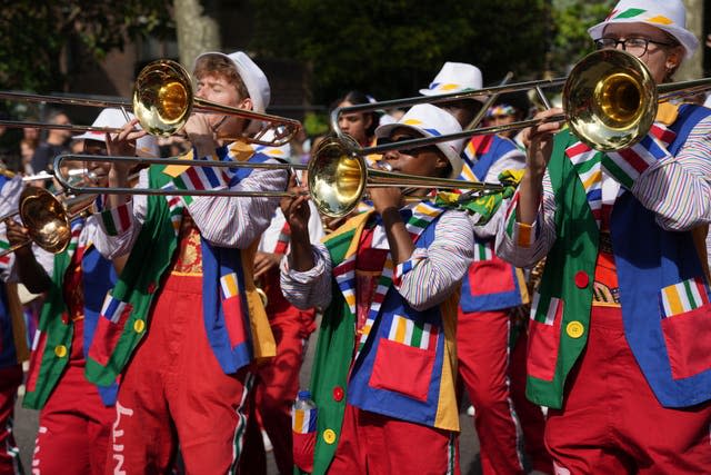 Children dressed in multi-coloured jackets blow trumpets as part of a band