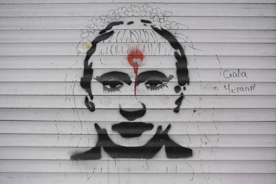 Graffiti depicting Russian President Vladimir Putin and the words "Glory to Ukraine" cover the blinds of a battle-damaged shop in Stoyanka, Ukraine, Sunday, March 27, 2022. (AP Photo/Vadim Ghirda)