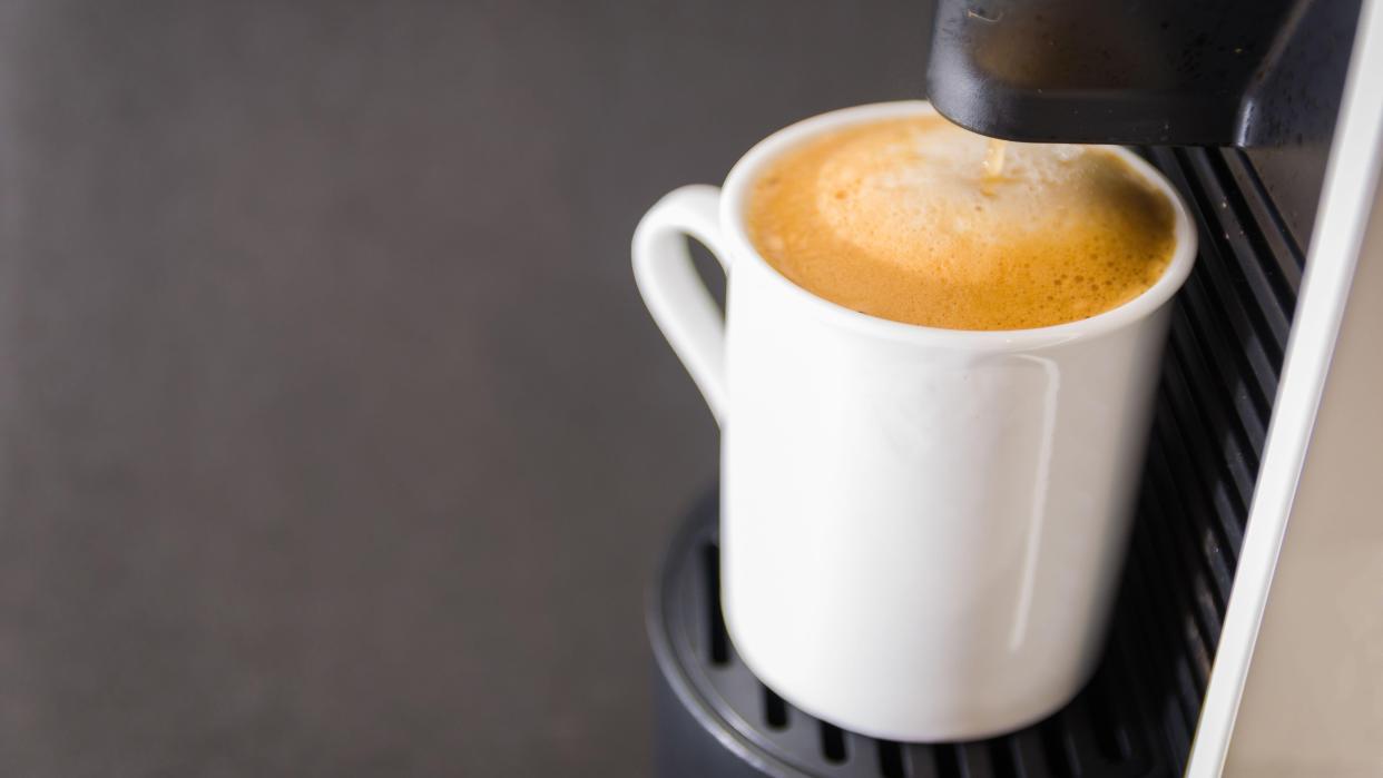  How to use a pod coffee machine: Machine brewing coffee into cup. 