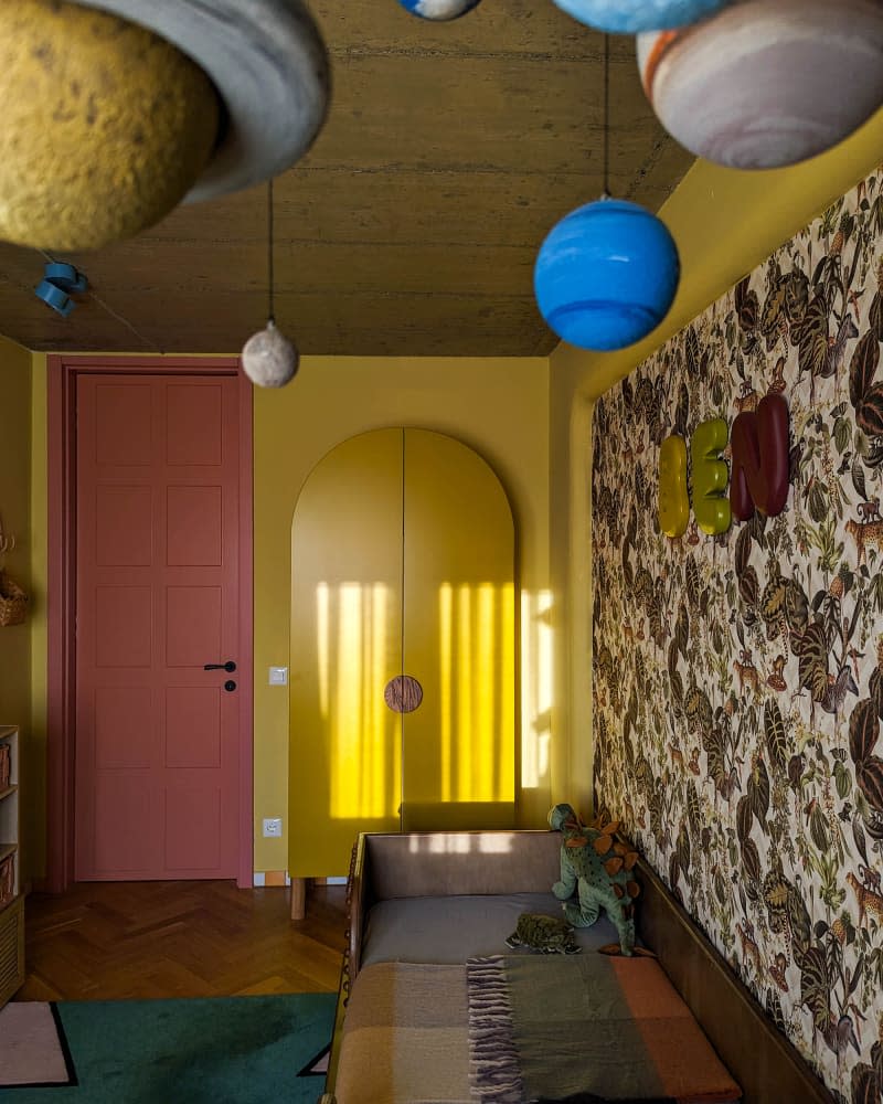 Yellow kids room with botanical wallpaper accent wall, brown leather and wood bed, yellow wardrobe, and solar system mobile