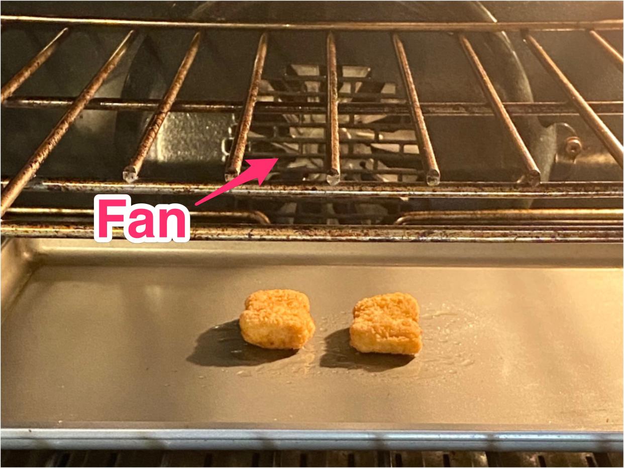 Two nuggets on a metal baking tray in an oven. You can see the convection fan in the back of the oven.