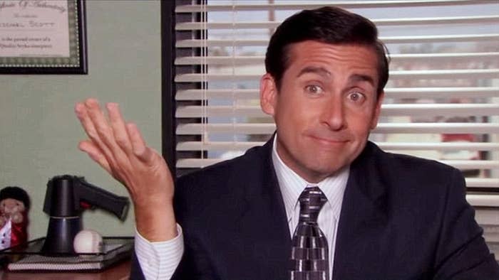 Man in business attire making a shrugging gesture at an office desk