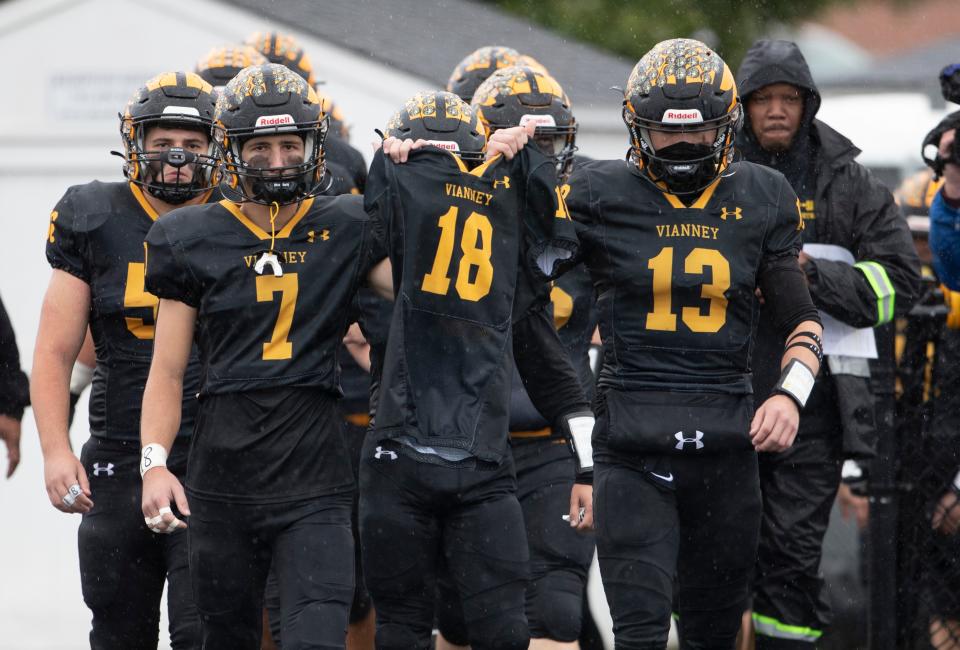 St. John Vianney's Jack Farrah's (No. 7)  and Kyle Verriest (No. 13) lead their teammates on to the field for Sunday's game against Marlboro holding the jersey of injured teammate Aaron Van Trease