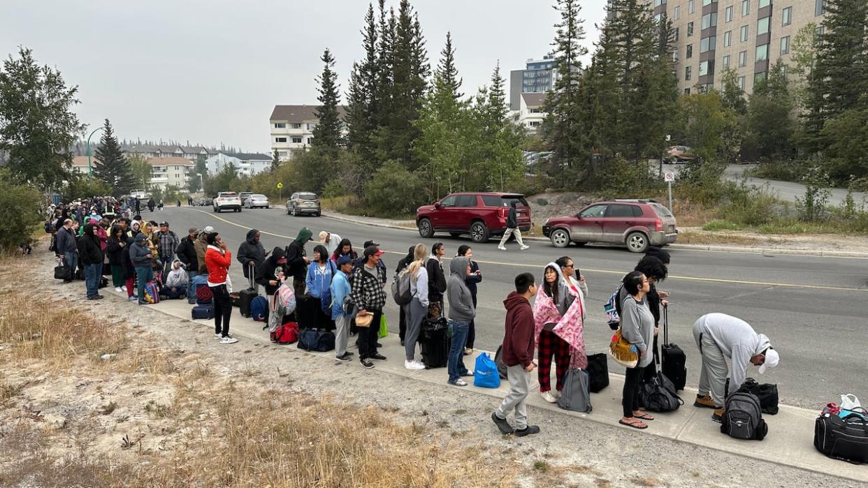 A line of people at Sir John Franklin High School, stretching down 49th Street, waiting to get on evacuation flights out of Yellowknife. The entire city has been ordered to evacuate by noon on Friday because of threatening wildfires. (Francis Tessier-Burns/CBC - image credit)