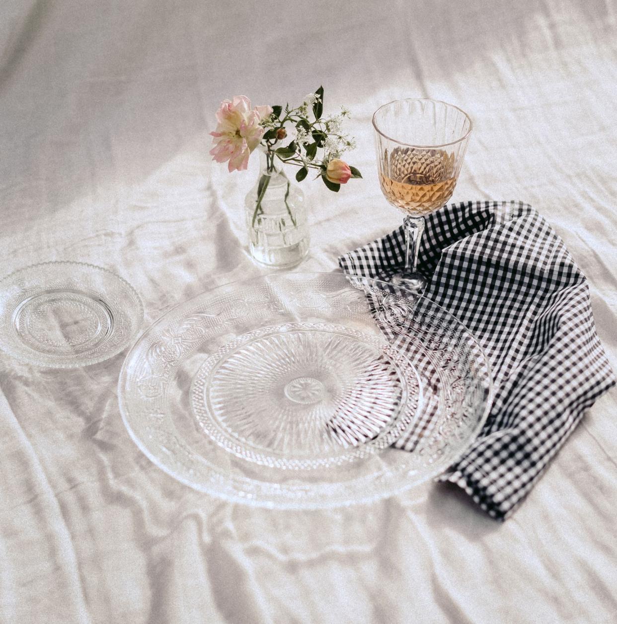 Decorative concept for wedding where we observe glass tableware on a white linen cloth. Blue checkered napkin. Flower vase. Wine glass.