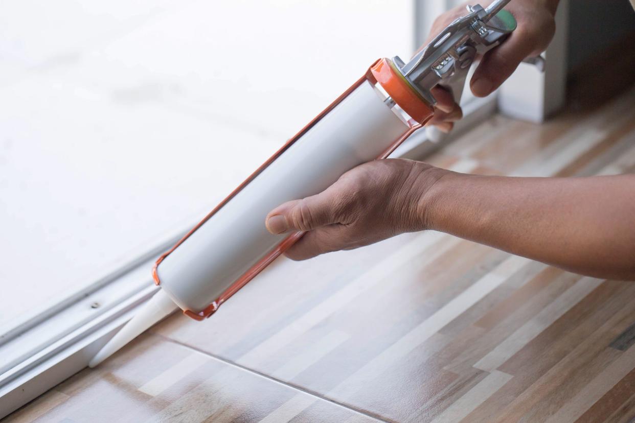 man's hand uses silicone adhesive with a glue gun to repair worn windows