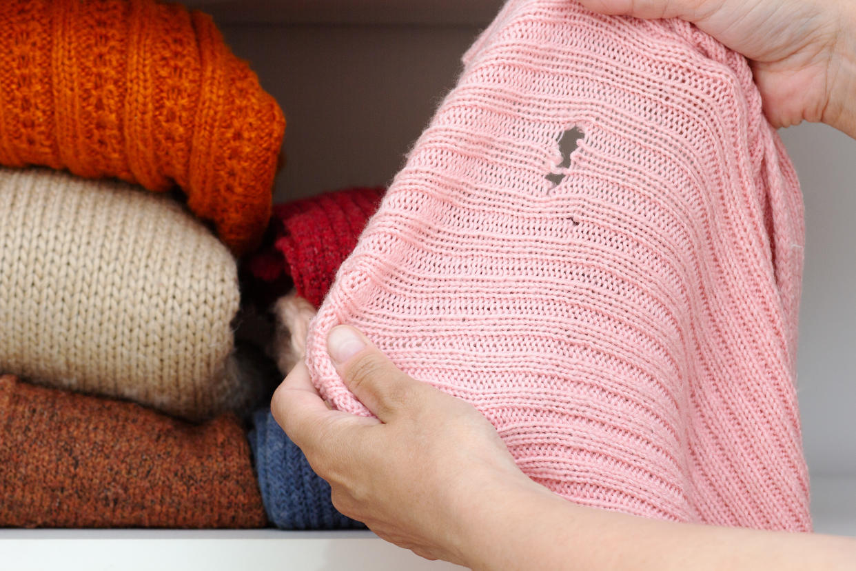  Person holding pink sweater with holes in in front of pile of folded sweaters iStock. 