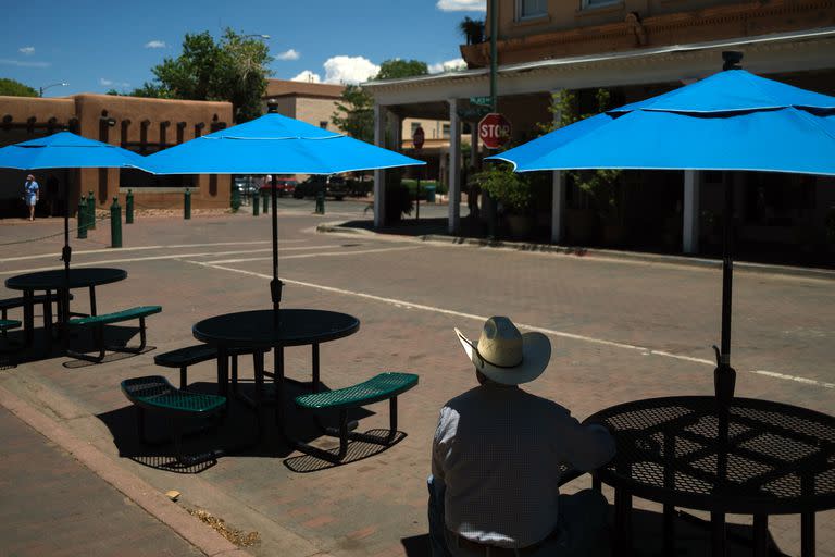 Un hombre se sienta a la sombra de una sombrilla en una Plaza de Santa Fe prácticamente desierta en Santa Fe, Nuevo México, el lunes 17 de julio de 2023.
