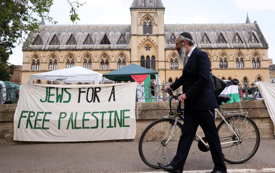 A man whose kippa suggests he is a Jew pushes his bicycle past a banner which reads 'Jews for a Free Palestine'