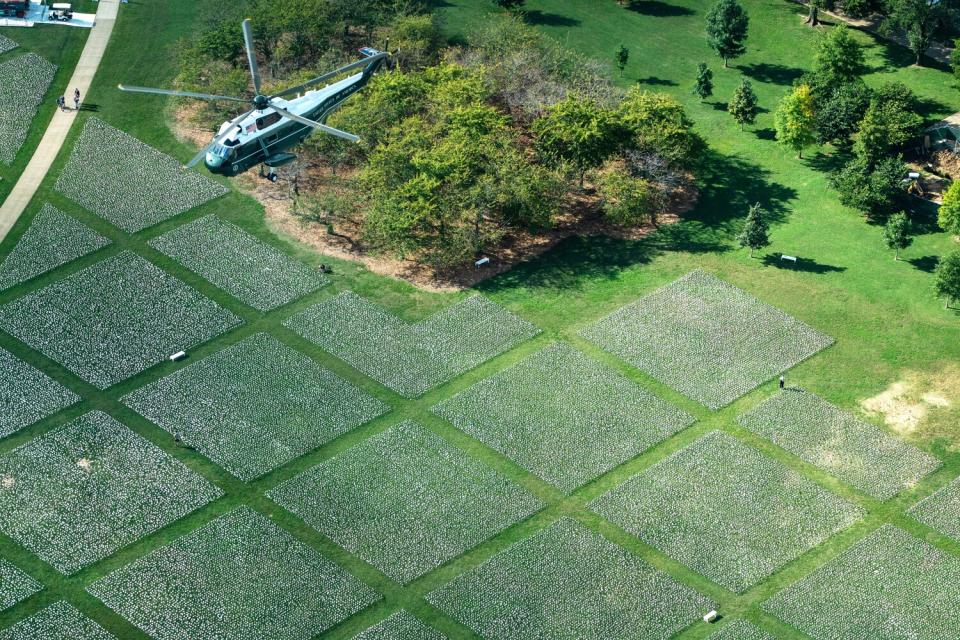 A helicopter flies above a grassy area covered in small white objects.