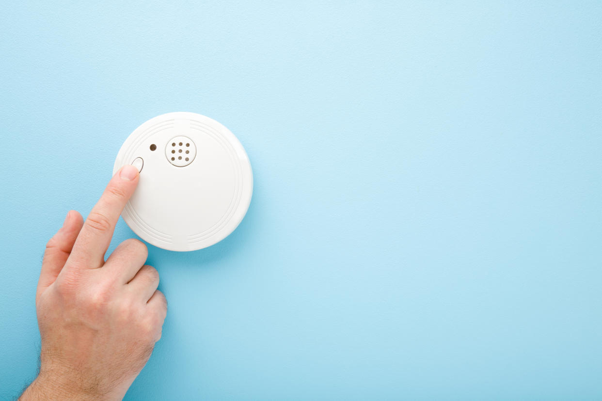 Young man finger touching new white plastic smoke alarm. Light blue table background. Pastel color. Safety concept. Empty place for text.